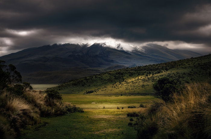 an image of a valley with dark clouds above and a light pool in the foreground