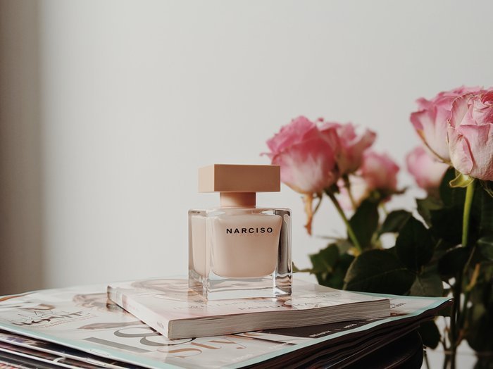 Product photo of perfume on a desk beside pink roses