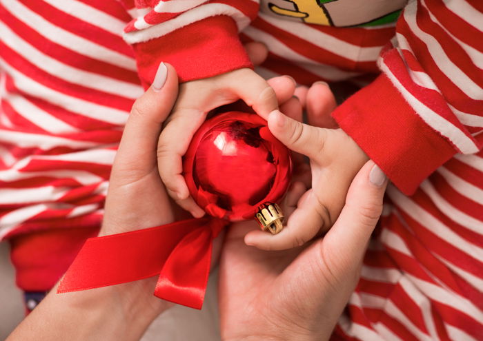 Close up of a couple holding their babies hands with a Christmas decoration