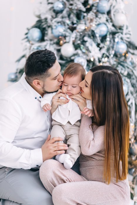 Sweet first Christmas photo of a couple holding their baby in front of the christmas tree