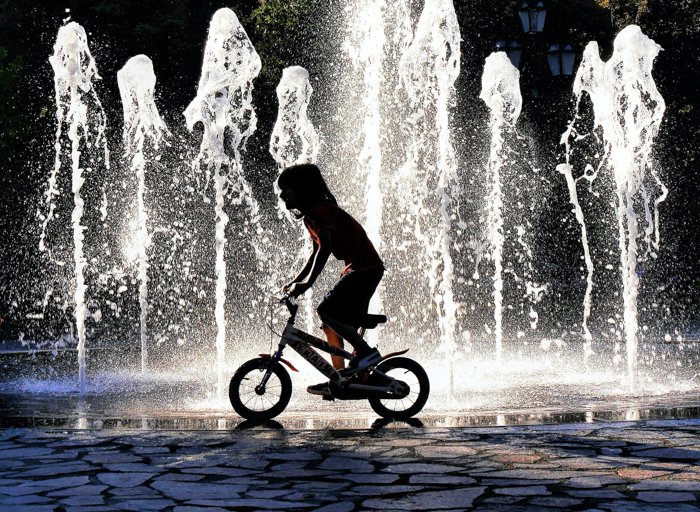 an image of a child riding their bike in front of a backlit fountain