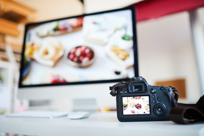 Background image of photo camera with photo of food on table against computer with editing software