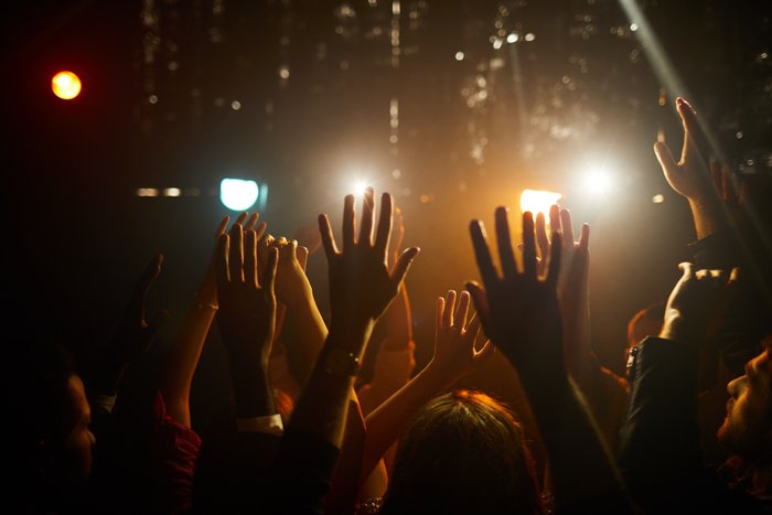 Crowd of people standing in dark club and waving hands in air