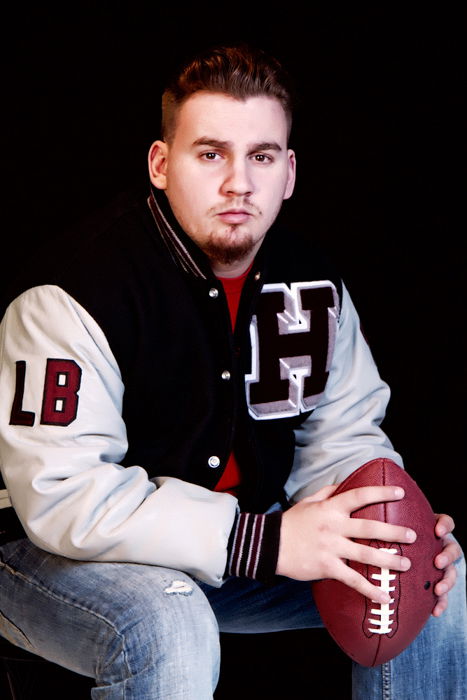 a young male poses while sitting down and holding a football