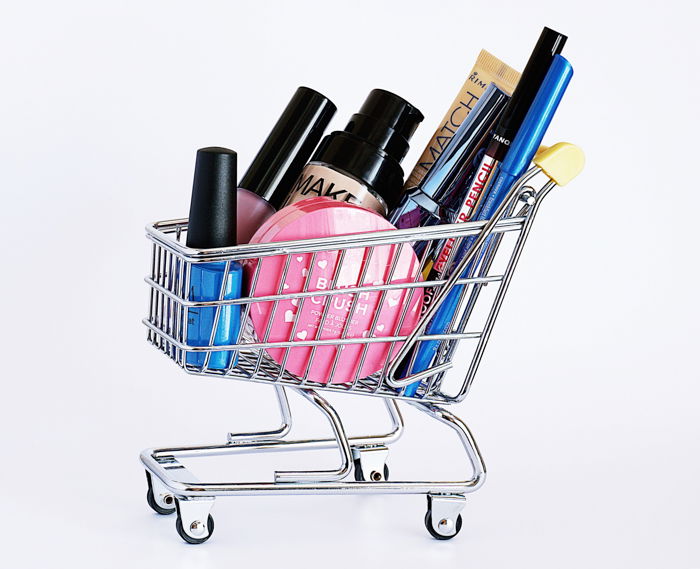 Product photography image of a miniature shopping cart with cosmetic products