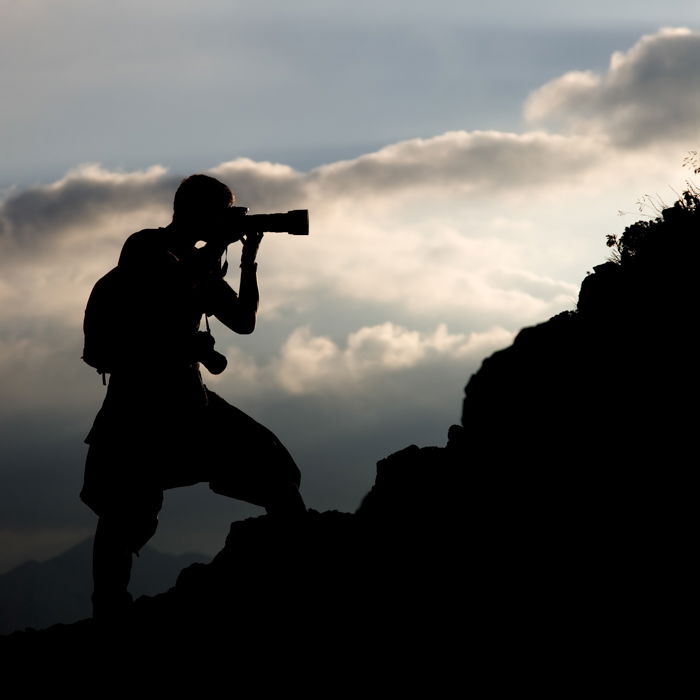 a silhueta de um homem em uma colina fotografando com uma lente teleobjetiva