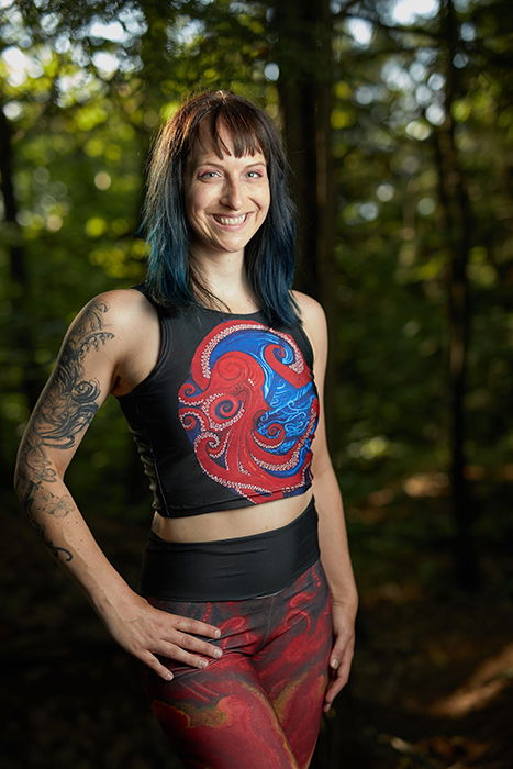 A woman stands confidently in front of a forest, posing for the camera. 