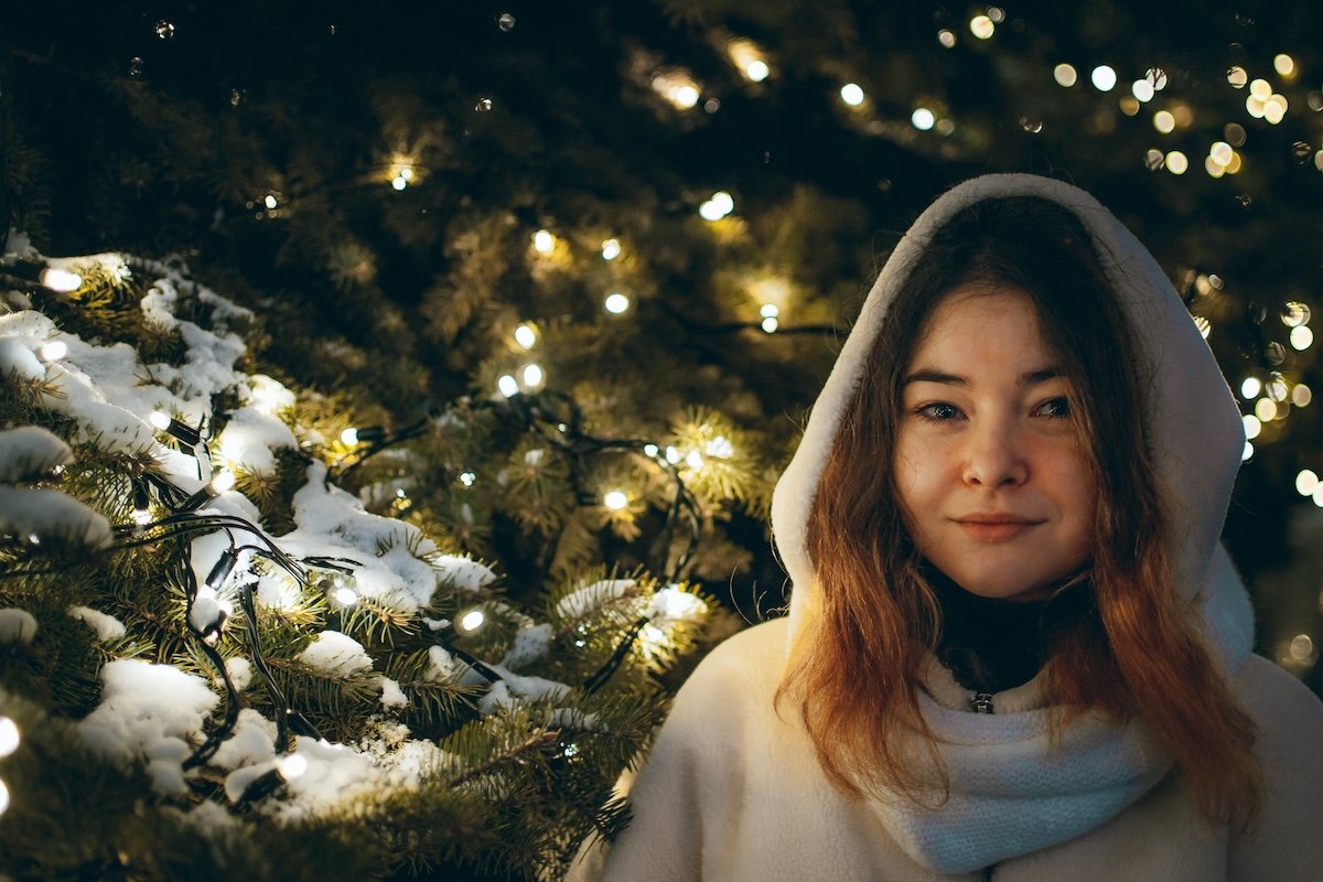 Portrait of a woman ina hooded turtleneck standing beside Christmas lights at night