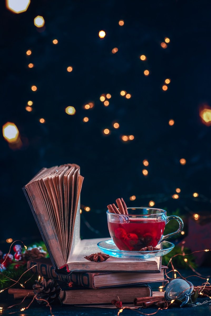 Still life of red berry tea on a stack of books with a dark background with Christmas lights