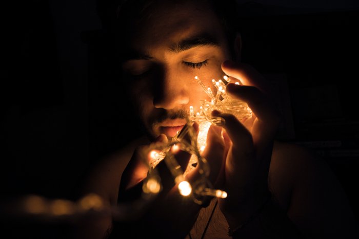 A portrait of a man holding a string of Christmas fairy lights to his face