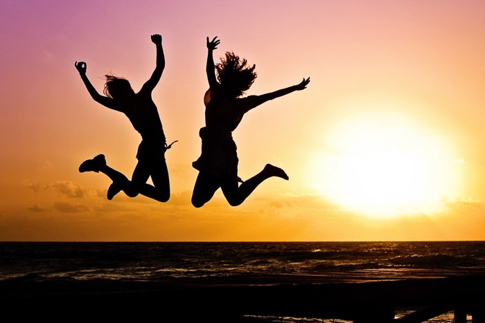 The silhouette of two girls jumping over the sea at sunset