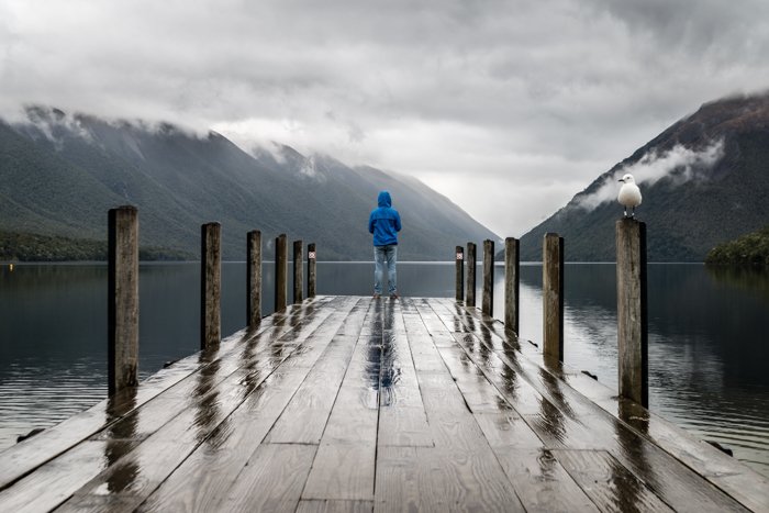 A person in a blue jacket standing on the end of a wooden pier