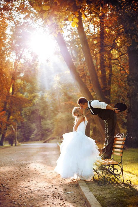 Atypical image of the groom standing up on a bench while giving a kiss to the bride