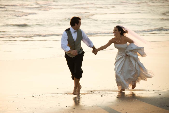 An image of the groom and the bride running at the beach