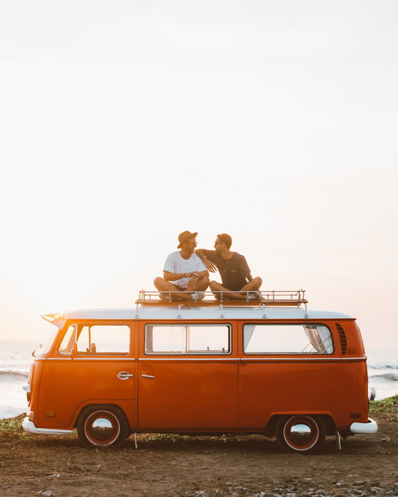 an image of two friends sitting on top of an orange volkswagen bus