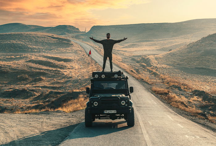 Fotografia de aventura de um homem de pé em um caminhão enquanto dirige pelo deserto.