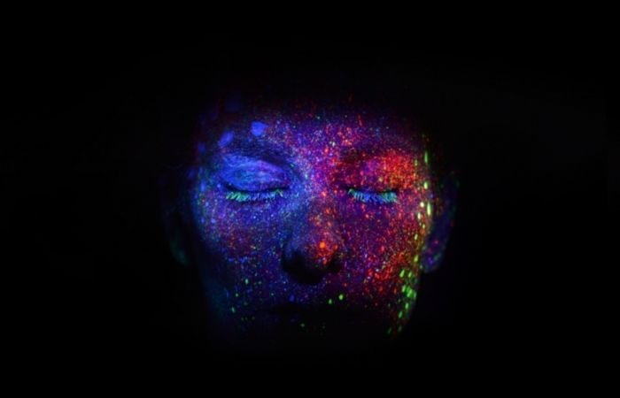 a close up conceptual portrait photo in black light of a face with paint