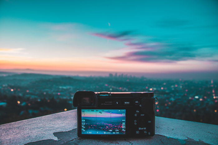 an image of a mirrorless camera set on a ledge overlooking a city skyline at dusk