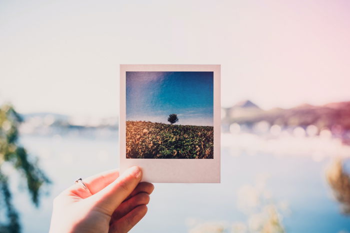 A imagem de uma mão segurando uma foto polaroid impressa perto da praia