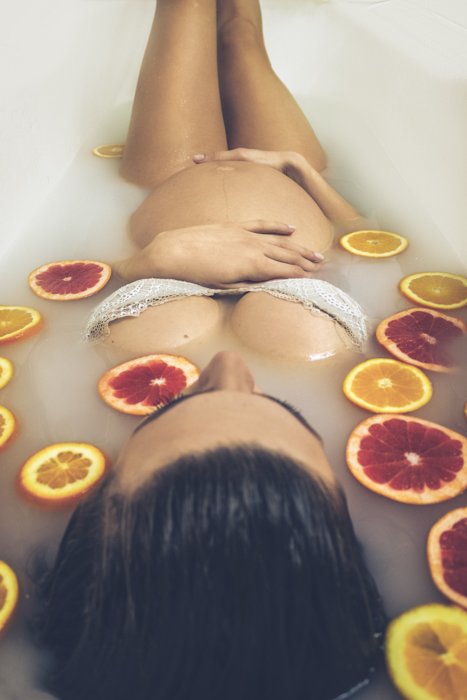 A boudoir photography of a pregnant woman in milk bath surrounded by grapefruits.