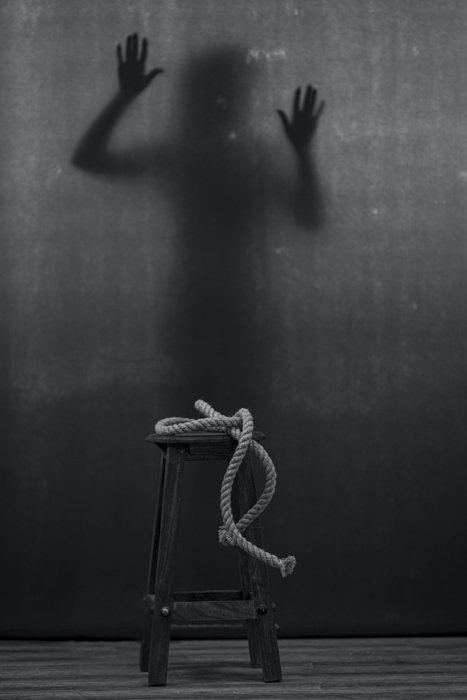 black and white image of a rope on a stool and a shadowy figure in the background
