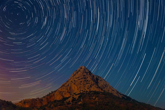 a time lapse image of the night sky behind a mountain