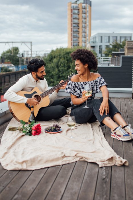 Image of a romantic couple doing picnic while the boyfriend is playing on a guitar