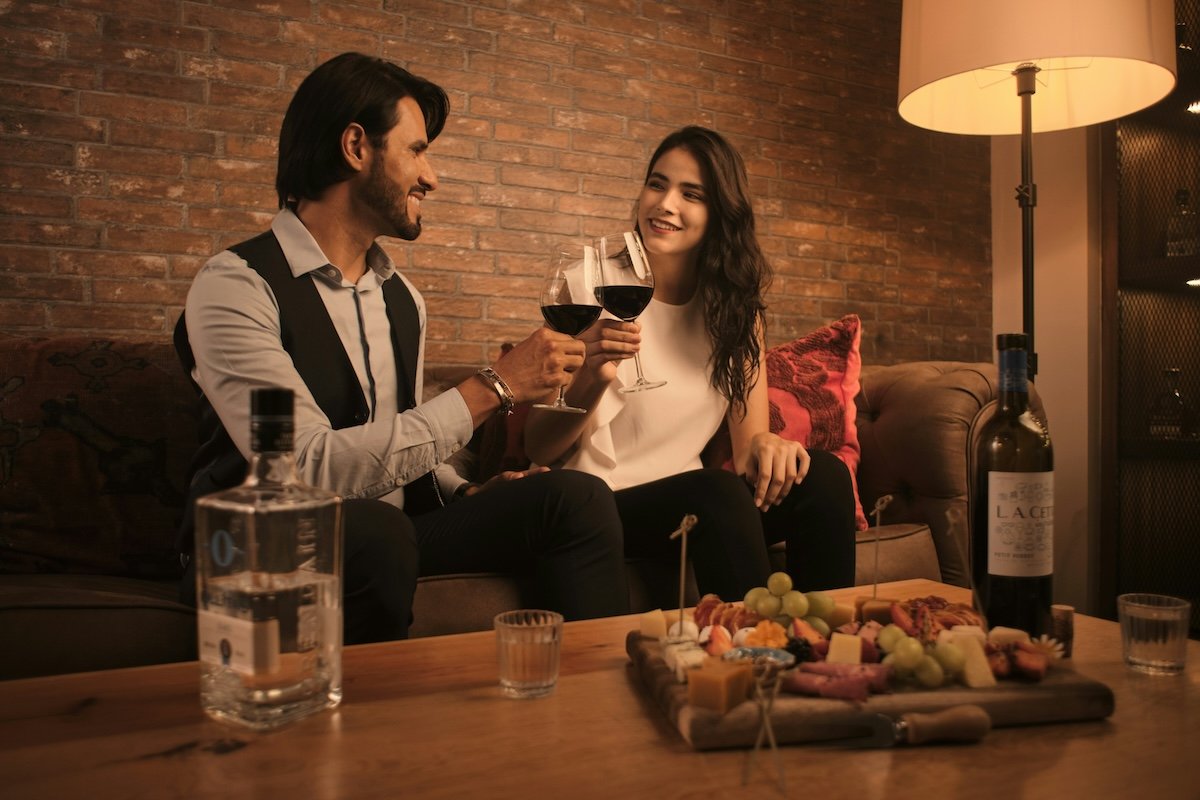 A couple sitting on a couch with wine and hors d'oeuvres for a Valentines day photoshoot idea