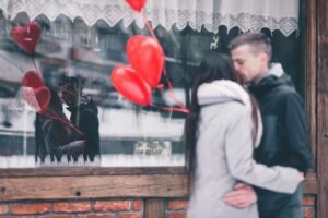 Couple embracing outside with heart balloons and reflection in a window as a Valentines day photoshoot idea