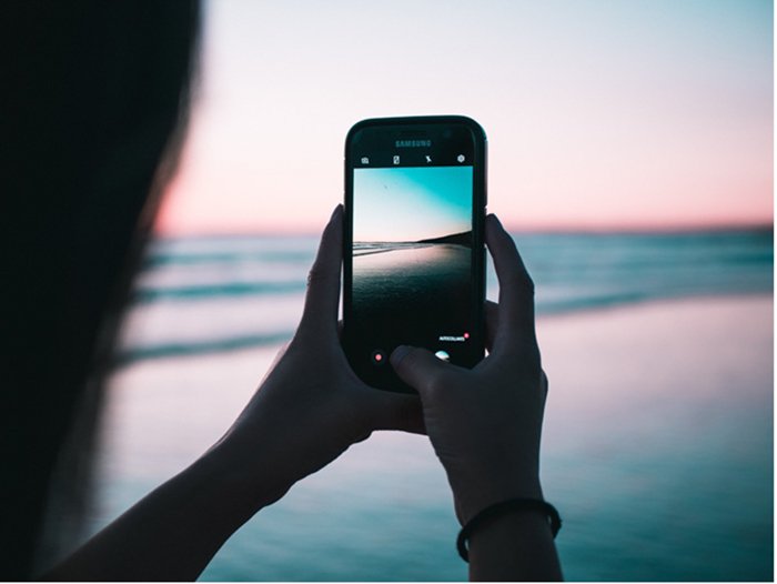 person taking smartphone photo at beach
