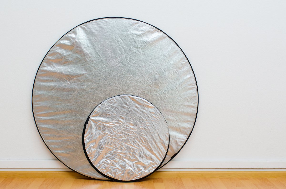 Two round silver reflectors against the white wall of a photo studio
