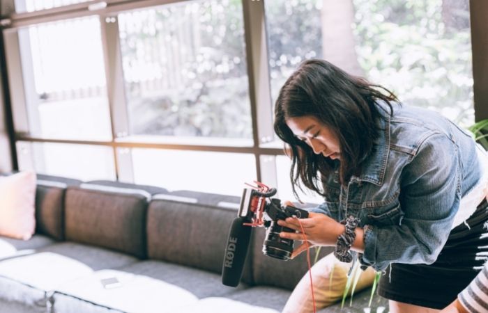 a woman sitting on a couch holding a camera with a hot shoe microphone