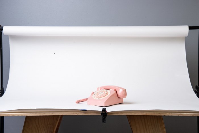 White seamless paper covering a table with a pink telephone on it