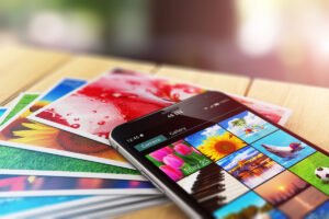 A smartphone with photos on its screen with a stack of photo prints
