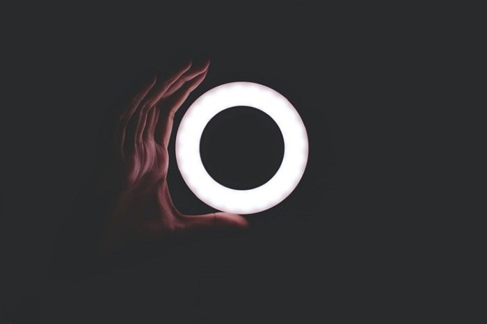 natural-toned ring light with a dark background and hand curved around it