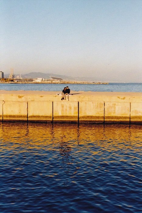 Couple sitting on a concrete pier above a blue sea
