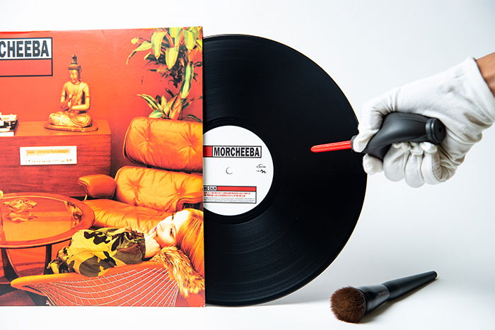 A hand using an air blaster to remove dust on a vinyl record