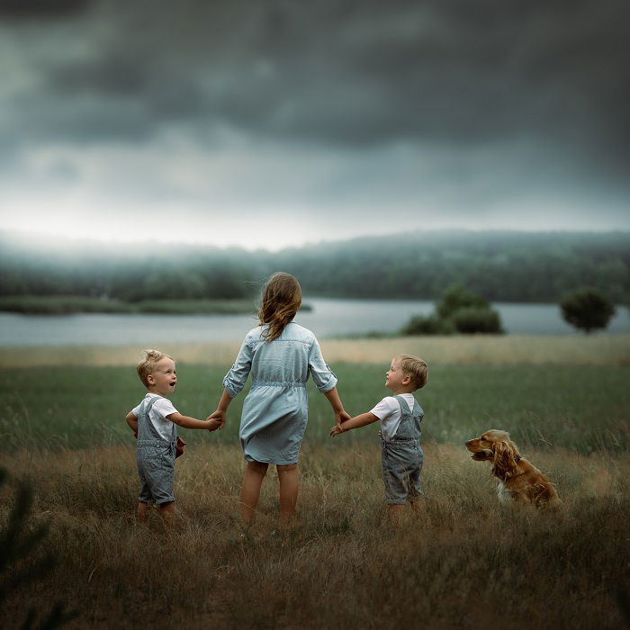 three kid poses with a dog in a dramatic countryside landscape