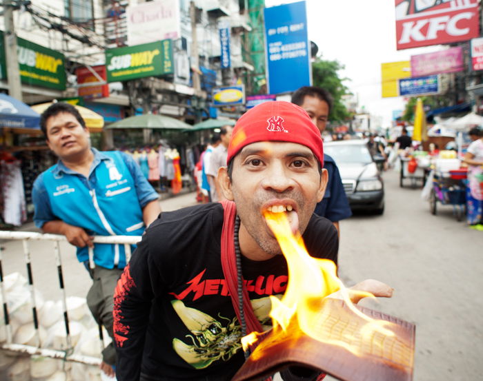 An environmental portrait photo of a street vendor in Bangkok demonstrating a fire-proof crocodile skin product