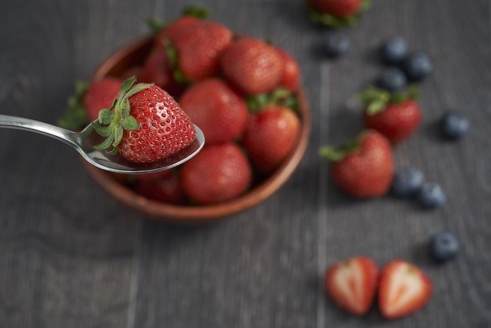 Full-frame sensor food-photography image of strawberries and blueberries with a blurred table and background