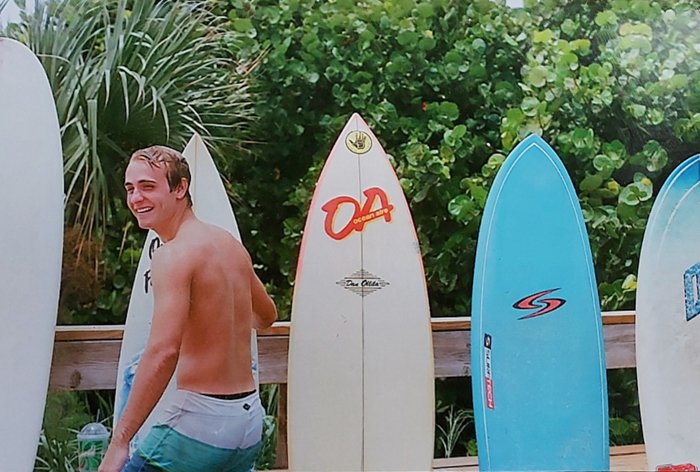 A scanned image of a surferposing in front of surfboards