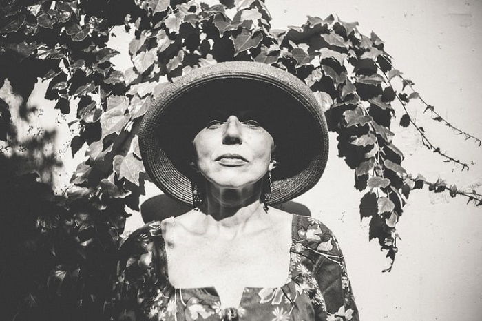 black and white film image of a woman wearing a hat and floral blouse
