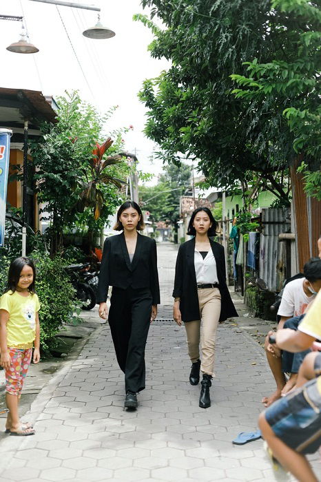 An editorial image of two fashion models walking down a residential neighbourhood sidewalk