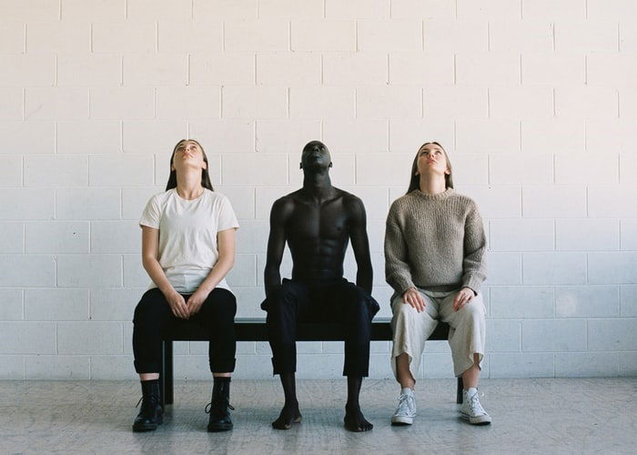 Editorial image of three people sitting on a bench and looking up with a white block cement wall behind them