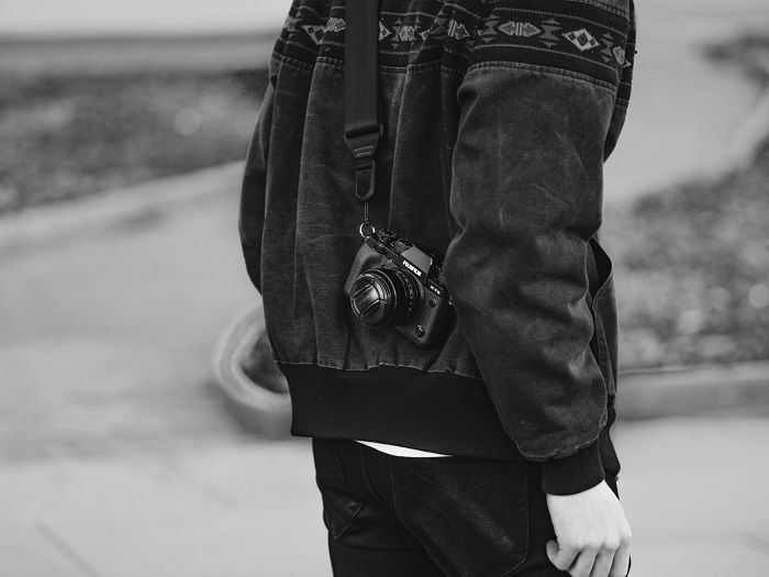 A black and white image of a Fujifilm camera slung over the shoulder of a male