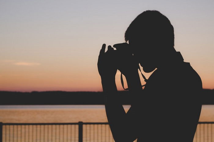 fotógrafo olhando para um corpo de água ao pôr do sol