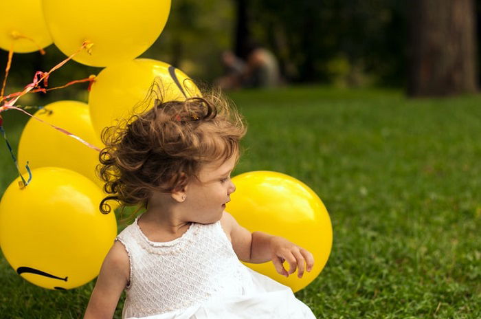 child photography in a candid shot with a green field and yellow balloons