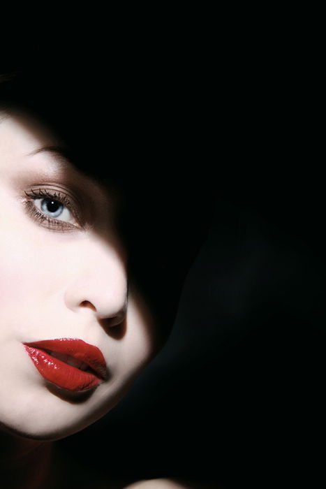 Portrait or a woman with white make-up red lips and a shadow across her face taken with hard light