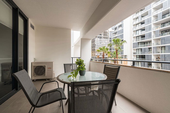 An apartment balcony with chairs, a table, and a view of buildings shot for real estate photography