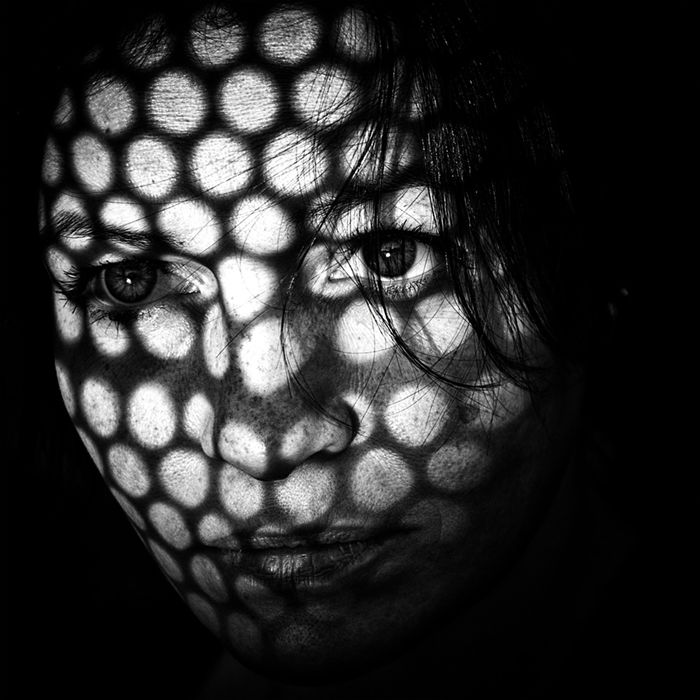 A portrait of a woman with a patterned grid of light and shadow illuminating parts other face